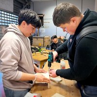 Zwei Auszubildende arbeiten an einer Holz-Werkbank.